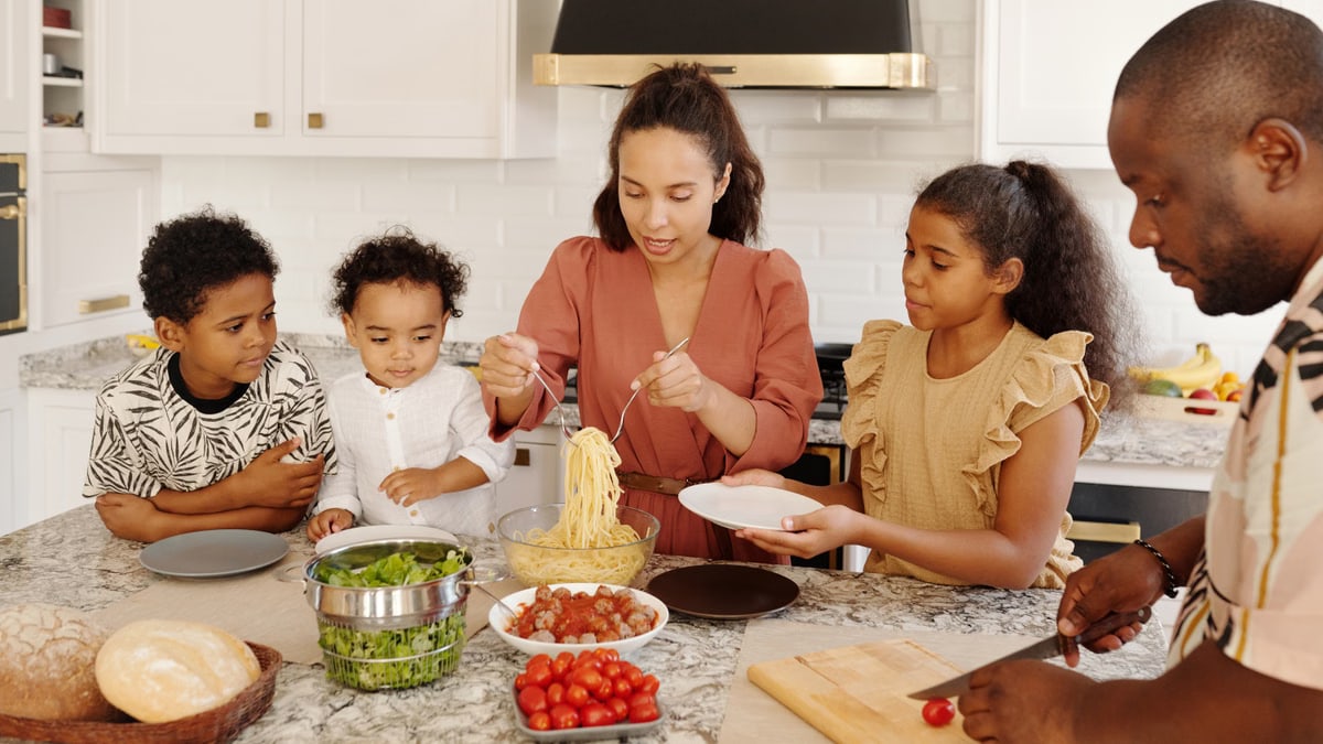 Family enjoying a cooking session together in a modern kitchen, preparing pasta and vegetables.